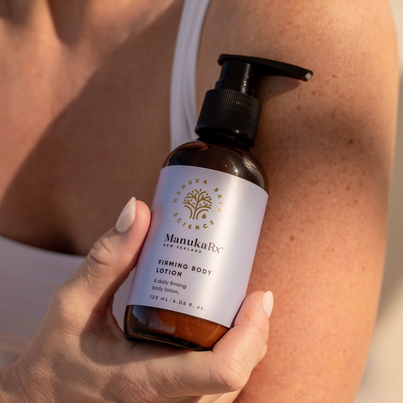 Hand holding ManukaRx bottle of Firming Body Lotion