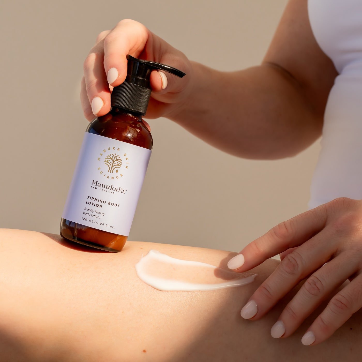 Woman holding bottle of ManukaRx Firming Body Lotion while applying product to her leg