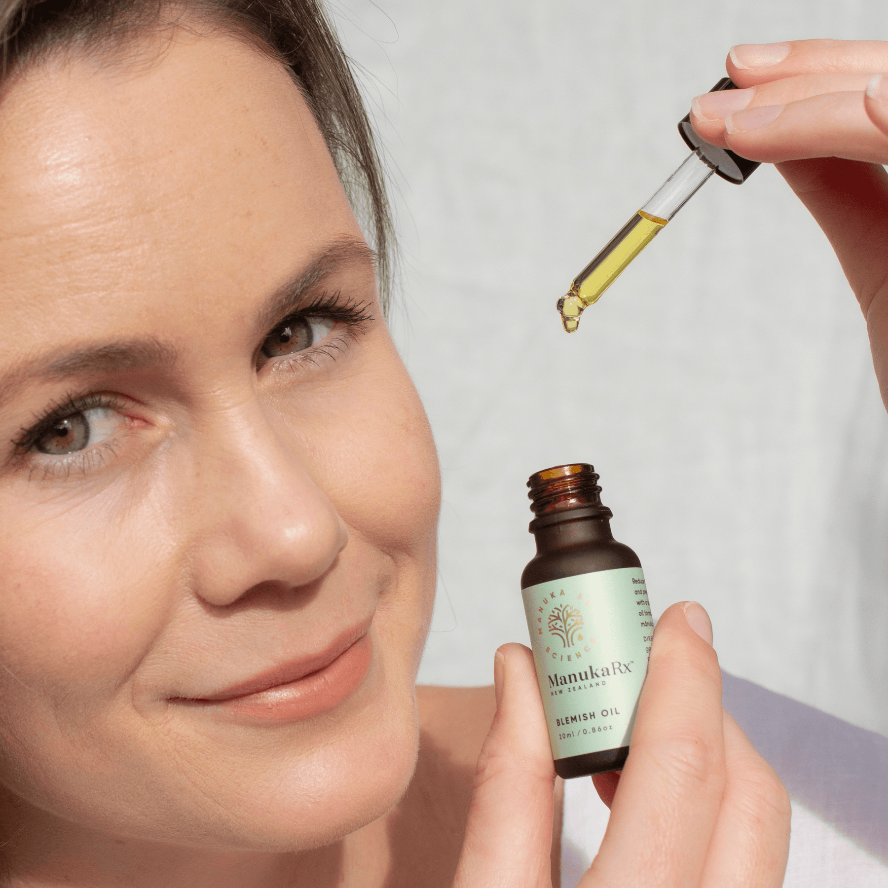 Woman holding ManukaRX Blemish Oil and dropper in hand