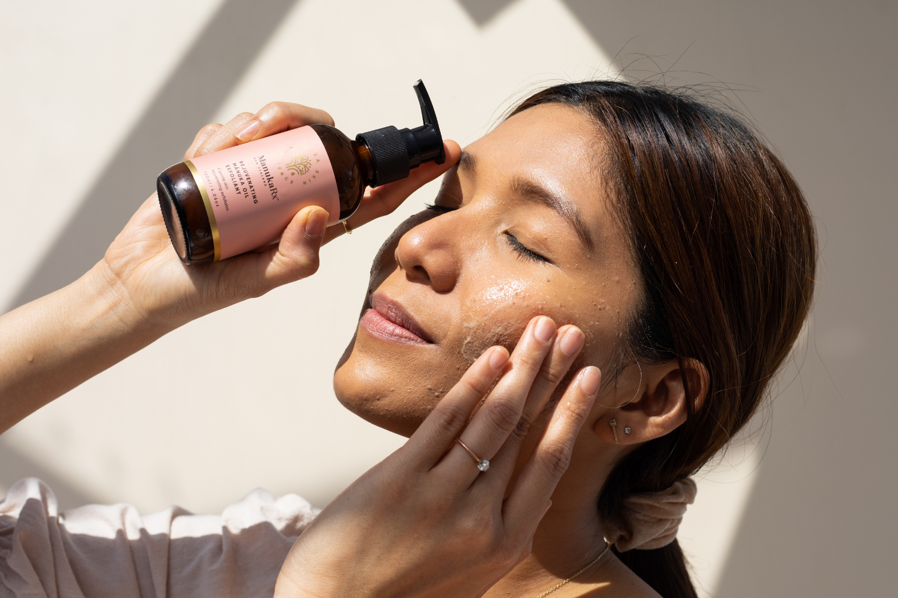 Woman holding bottle of ManukaRx Rejuvenating Mānuka Oil Exfoliant