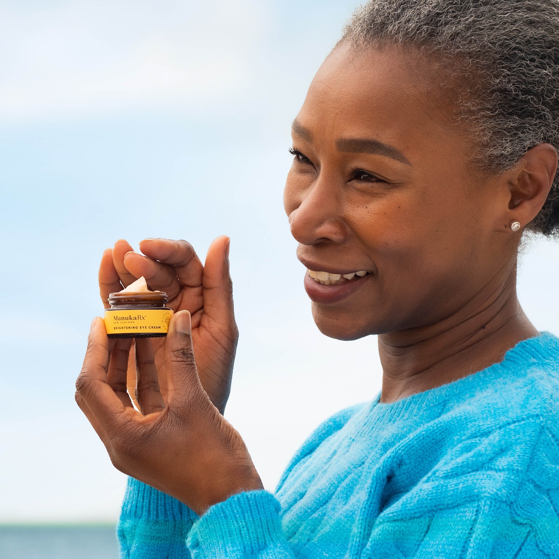 Woman holding jar of ManukaRx Vitamin C Brightening Eye Cream